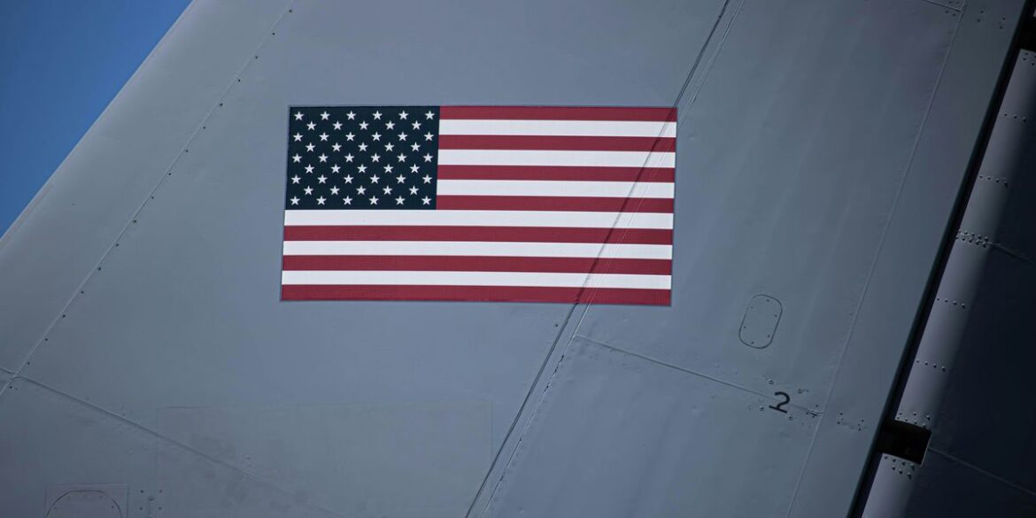 American flag on the side of a gray aircraft tail under blue sky.jpg