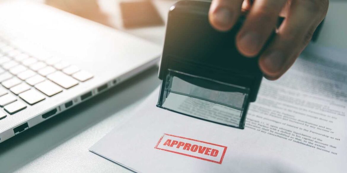 Hand stamping approved on document beside laptop on desk.jpg