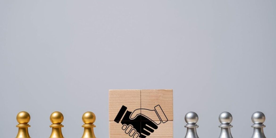 Gold and silver pawns flank wooden blocks with a handshake illustration.jpg