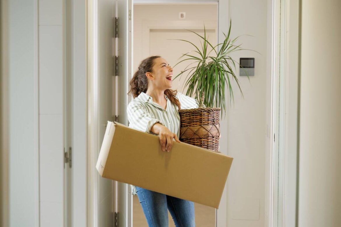Happy Single pretty young adult woman arriving entering the door of her new moving house with boxes.jpeg