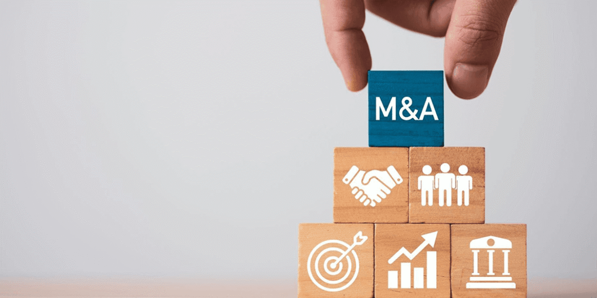 Hand places a blue block labeled m a atop a pyramid of wooden blocks with business icons.png