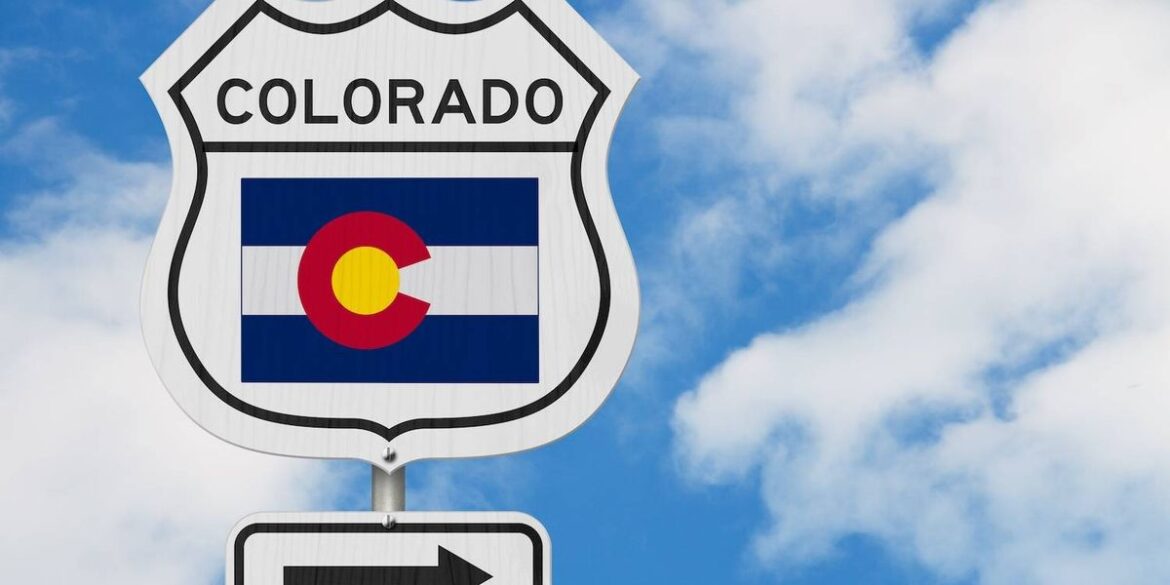 A road sign displaying the colorado flag and an arrow set against a blue sky with white clouds.jpg