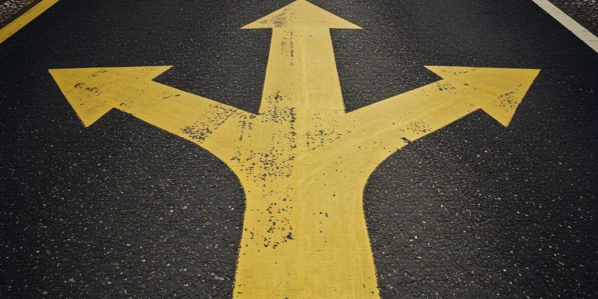Bold yellow three directional arrow painted on a textured black asphalt road.jpg
