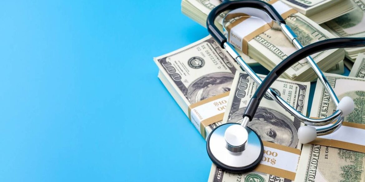 Stethoscope rests on stacks of us money over a bright blue background.jpg