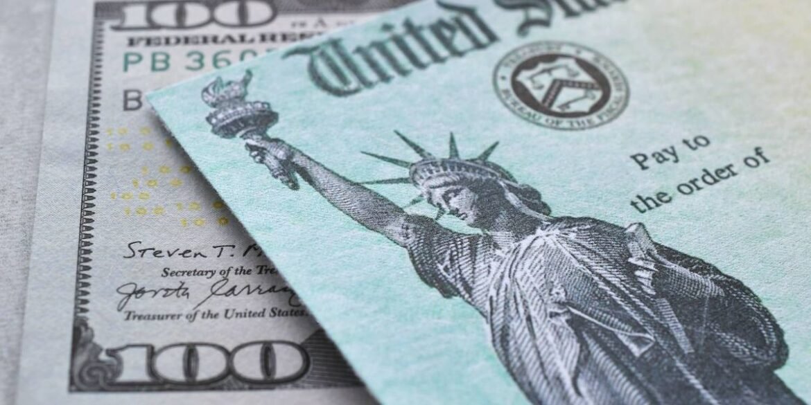 A u s treasury check with the statue of liberty is placed over a one hundred dollar bill.jpg
