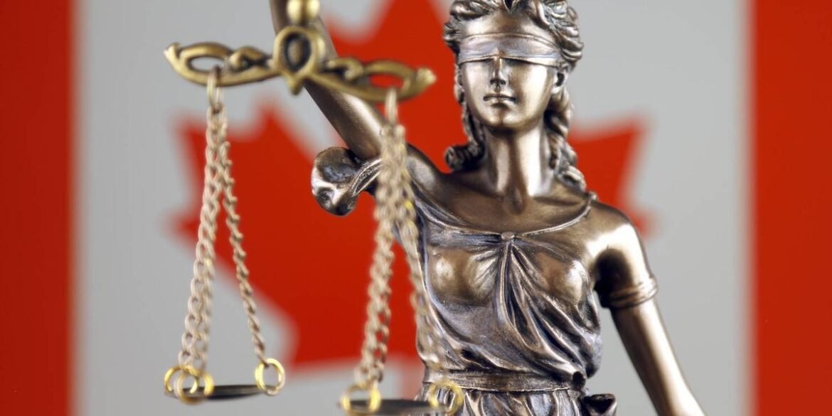 Bronze statue of lady justice holding scales in front of a blurred canadian flag background with red.jpeg