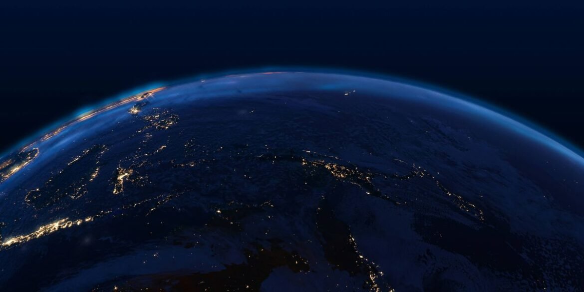 The dark earth horizon displays glowing city lights under a deep blue sky in a nighttime view from s.jpeg