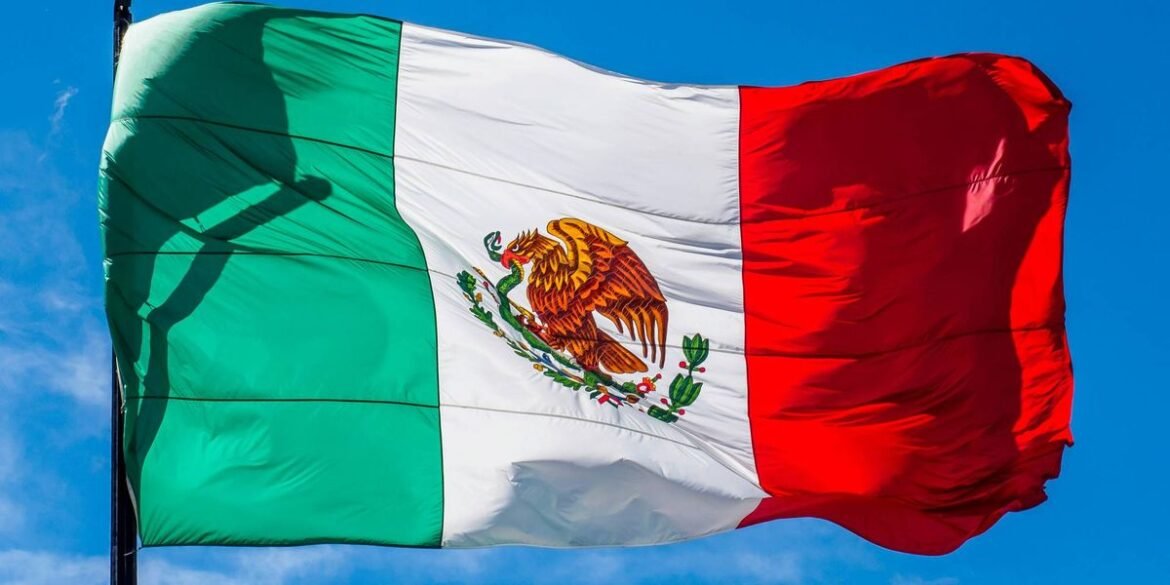 The mexican flag with green white and red stripes waves against a blue sky.jpg
