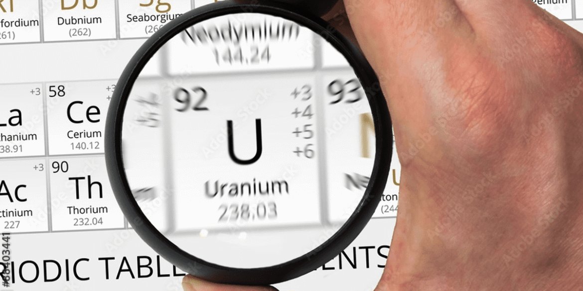 Hand holding magnifying glass over uranium on periodic table.png